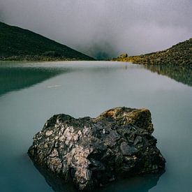 Mountain lake at glacier with rock in Caucasus mountains in Georgia on grey, dark day by Robin Patijn