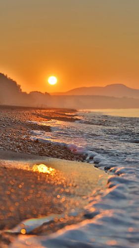 Zonsopkomst met bergen op de achtergrond en golven op de voorgrond.