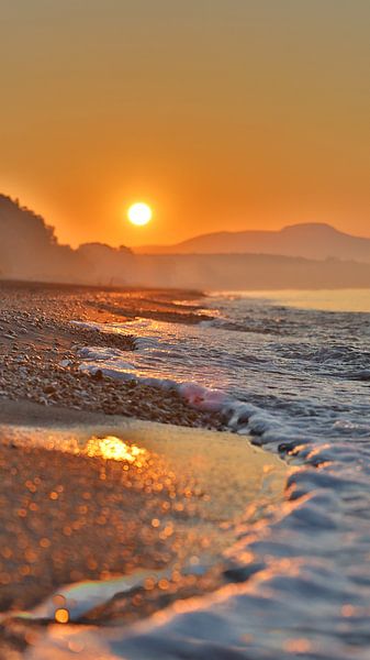 Lever de soleil avec des montagnes en arrière-plan et des vagues au premier plan. par Angela Seubring