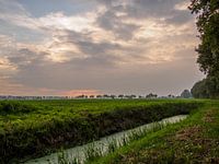 Sloot langs weide bij zonsondergang