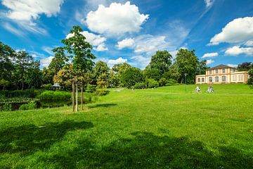 Mooi park in de lente met klein kasteel op groene heuvel voor blauwe hemel met witte wolken van pixxelmixx