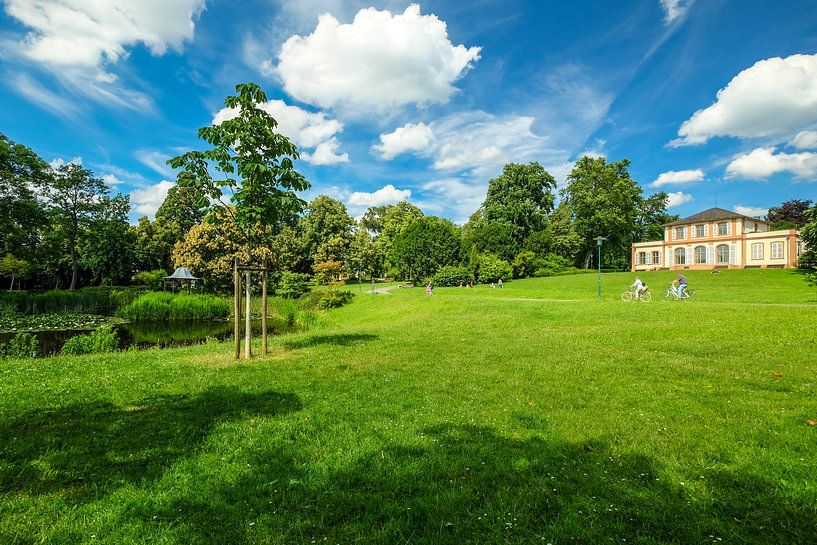 Beautiful park in spring with little castle on green hill in front of blue sky with white clouds by pixxelmixx