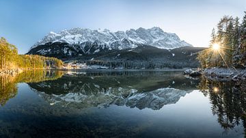 Eibsee in winter with snow and Zugspitze. Sun shines through the trees at sunset. Bavaria. Germany