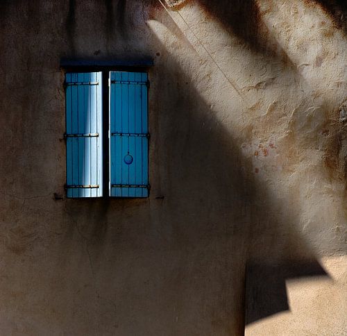 Blauwe luiken in een lichtbruine door de zon beschenen muur....