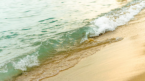 Een turkooizen oceaangolf die op een goudkleurig zandstrand breekt