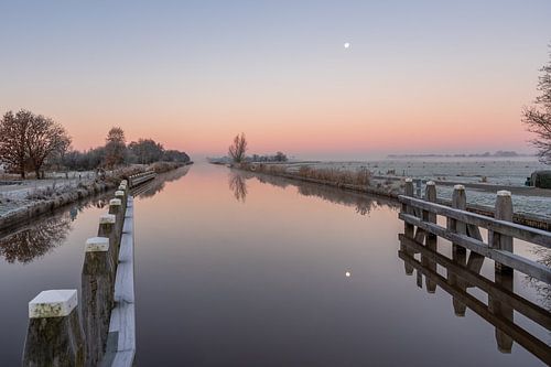 Een kanaal met reflectie van de volle maan tijdens zonsopkomst.