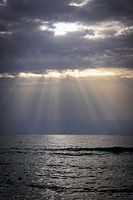 Strand met zee en dreigende lucht met zonnestralen van zonsondergang op Kreta, Griekenland