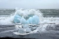 Blue ice floe on volcanic beach near Jokulsarlon. A wave breaks around it.