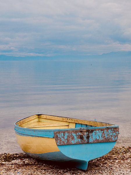Bootje in geel en blauw, eenzaam aan een meer van Judith van Wijk