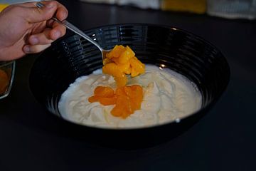 Spatel de mandarijnen met een lepel door het kwark- en yoghurtmengsel in een kom.