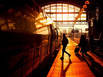Rezigers lopen over perron naar trein tijdens zonsondergang van Rob Kints