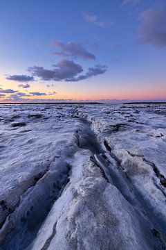 IJs bedekt de Waddenzee in de winter aan de Groningse Waddenkust tijdens zonsondergang. De ondergaan van Bas Meelker