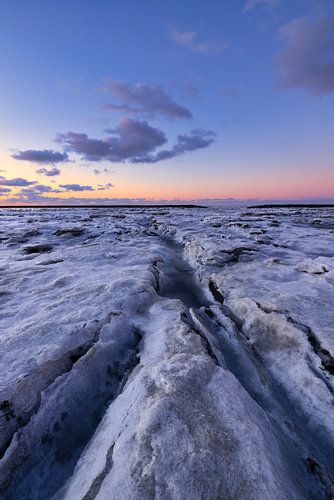 IJs bedekt de Waddenzee in de winter aan de Groningse Waddenkust tijdens zonsondergang. De ondergaan