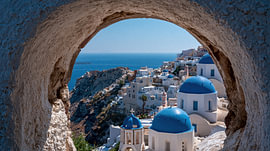 Ein Blick auf Santorini – Die blauen Kuppeln von Oia durch ein Stuckfenster