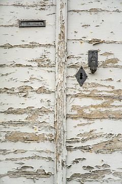 Oude witte deur waar de verf eraf aan het bladderen is. van Frans Scherpenisse