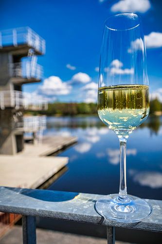 Close-up van een glas sprankelende champagne dat het duikplatform weerspiegelt, blauwe lucht en wolk