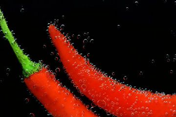 Rode paprika's staan onder water met luchtbellen tegen een zwarte achtergrond