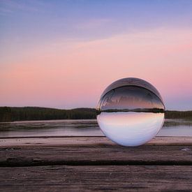 Glass ball on a footbridge reaching into a lake by Martin Köbsch