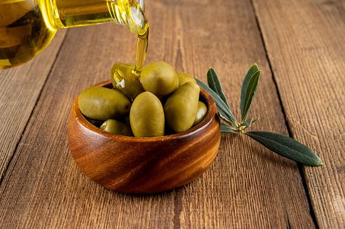 Olive oil and green olives in wooden bowl