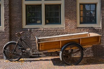 Oude houten bakfiets geparkeerd voor een historisch huis van Frans Rombout