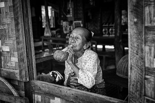 Old woman smokes traditional cheroot cigar in front of her home in Baghan in Myanmar by Wout Kok