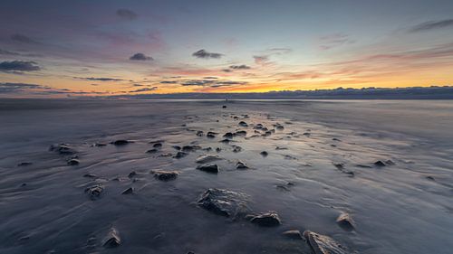 Een weidse blik op de Noordzee, waar de pier langzaam tevoorschijn komt wanneer de zee zicht terugtrekt tijdens een kleurrijke zonsondergang