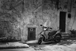 Scooter en noir et blanc devant un mur rustique dans une ville d'Italie sur iPics Photography