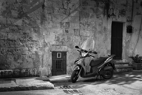 Scooter en noir et blanc devant un mur rustique dans une ville d'Italie sur iPics Photography
