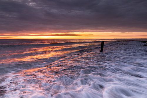 Golven overspoelen de zeepier tijdens een kleurrijke zonsondergang in Den Helder