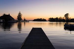 Une jetée sur l'eau calme au bord d'un lac avec le reflet du coucher de soleil et les silhouettes de