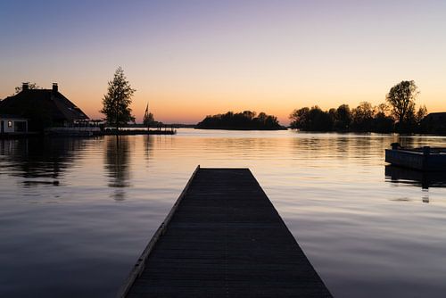 Een pier over rustig water aan de oever van een meer met reflectie van de zonsondergang en silhouett