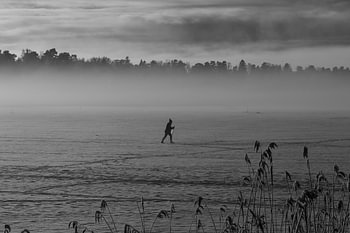 A lone skier crosses a frozen lake shrouded in mist.