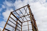 Urbex - verroeste metalen constructie tegen een blauwe lucht met wolken