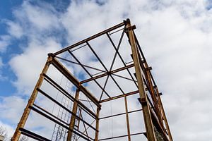 Urbex - verroeste metalen constructie tegen een blauwe lucht met wolken
