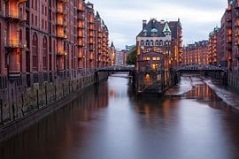 Hamburg’s Speicherstadt with the Wasserschloss. Lights glow against the evening sky. by Jiri Viehmann