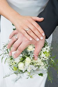 Mains d'un couple de mariés sur le bouquet de la mariée