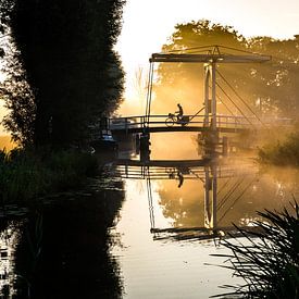 Lone newspaper delivery man cycles across a bridge in IJlst Friesland. One2expose Wout Kok Photograp