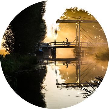 Eenzame krantenbezorger fietst over een brug in IJlst Friesland. One2expose Wout Kok Photography. van Wout Kok