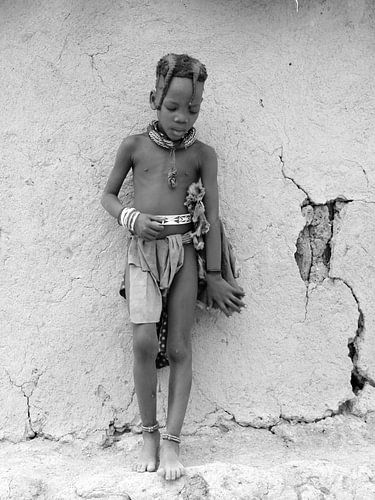 Himba kind tegen de muur van de hut.