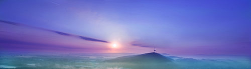 Sunrise over a mist-shrouded valley in shades of violet and turquoise, panoramic view