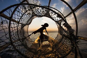Visser die met traditionele boot op het Inle meer in Myanmar op ouderwetse wijze met een vis korf vi