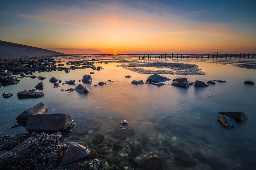 Wadden sunset with stones and poles by Jan Georg Meijer