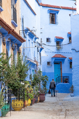 Man with a walking stick in a pastel-blue alleyway in Chefchaouen