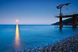 Sunset over the sea, a small crane on the pier, surf the lunar path. by Michael Semenov