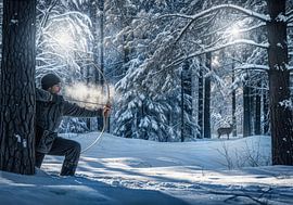 Mann mit Pfeil und Bogen zielt im verschneiten Wald auf ein Reh von Markus Gann