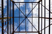 Urbex symmetrie - verroeste metalen constructie tegen een blauwe lucht met wolken