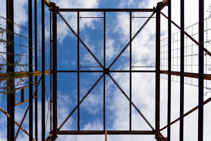 Urbex symmetrie - verroeste metalen constructie tegen een blauwe lucht met wolken van Photo Henk van Dijk