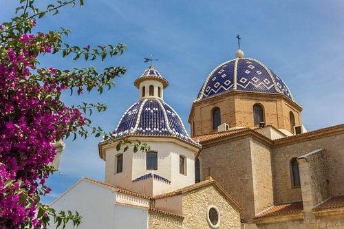 Pink flowers in front of the blue domes of the church in Altea