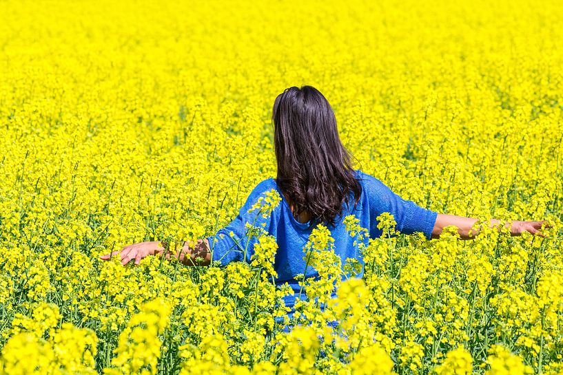 Young colombian woman walking in field with yellow rapeseed flowers by Ben Schonewille
