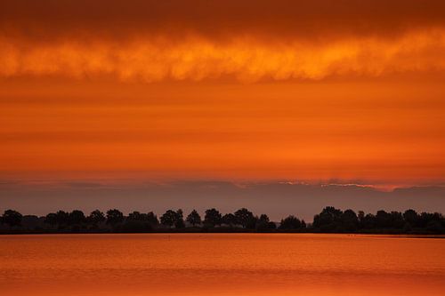 Een landschap van ochtendrood, het  rood weerspiegelt in het water.